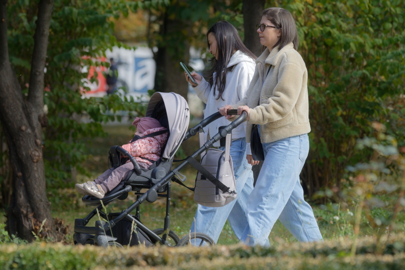 20 - Two women walking outdoors in a park with a modern stroller carrying a young child